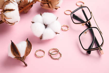 Branch of beautiful cotton flowers, eyeglasses and stylish jewelry on color table, closeup
