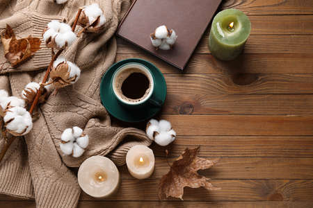 Cup of coffee, book, burning candles, warm sweater and beautiful flowers on wooden backgroundの写真素材