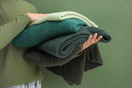 Woman holding stack of warm sweaters on green background