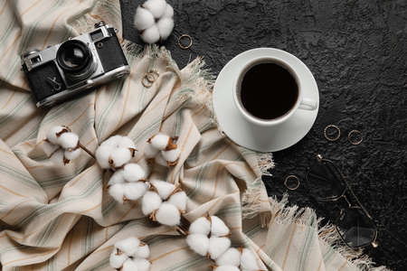 Cup of coffee, stylish jewelry, photo camera, cotton flowers and fabric on dark backgroundの写真素材