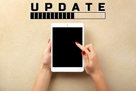 Hands with tablet computer, word UPDATE and status bar on beige background, top viewの写真素材