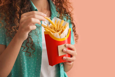 Young African-American woman with french fries on color background, closeup
