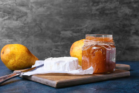 Glass jar of tasty pear jam and cheese on dark backgroundの写真素材