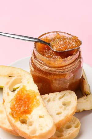 Glass jar of tasty pear jam and bread on pink background, closeupの写真素材