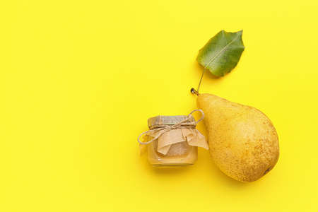 Glass jar of tasty pear jam on yellow backgroundの写真素材