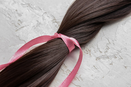 Brunette hair strand for donation with pink ribbon on grunge background, closeupの写真素材
