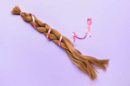 Braided red hair for donation with pink ribbon on lilac backgroundの写真素材
