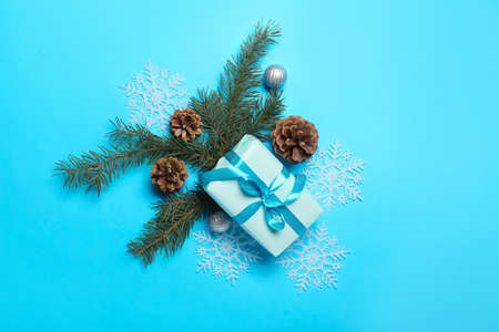 Christmas composition with gift box, pine cones and fir branches on blue background