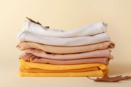 Stack of baby clothes and autumn leaves on color backgroundの写真素材