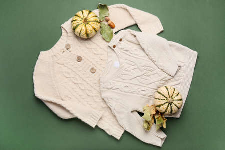 Stylish baby clothes and ripe pumpkins on green background