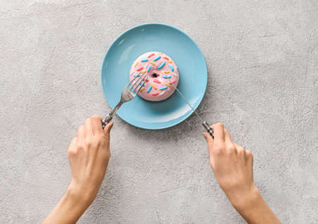 Woman eating delicious donut on gray backgroundの写真素材