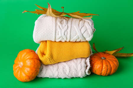 Stack of baby clothes, pumpkins and leaves on color backgroundの写真素材