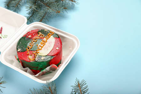 Plastic lunch box with tasty Christmas bento cake and fir branches on blue background