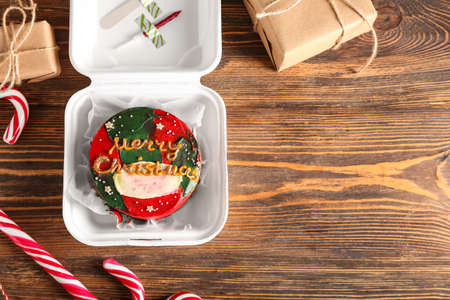 Plastic lunch box with Christmas bento cake, gifts and candies on wooden background