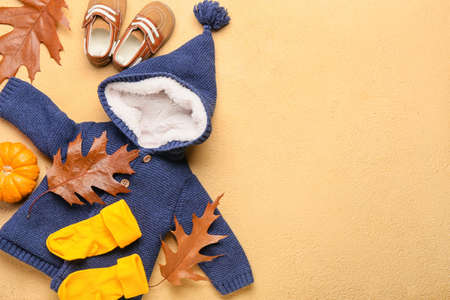 Stylish baby clothes, shoes, pumpkin and autumn leaves on color backgroundの写真素材