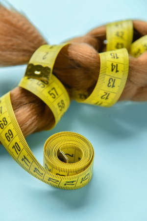 Braided red hair for donation with measuring tape on blue background, closeup