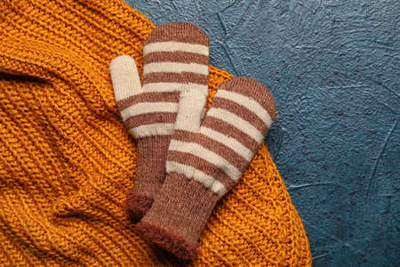 Pair of warm mittens and clothes on dark color background, closeup