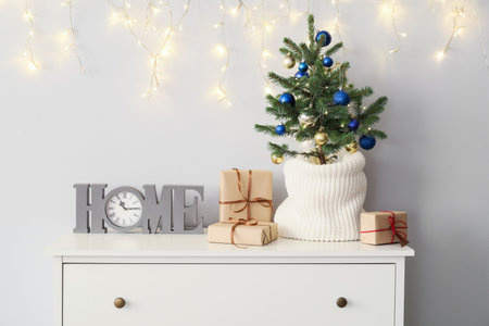 Small Christmas tree with gifts and clock on shelf near light wallの写真素材