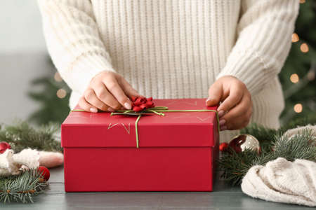 Woman decorating beautiful Christmas gift box at table in room, closeupの写真素材