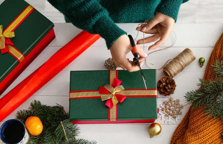 Woman decorating Christmas gift box at table in room