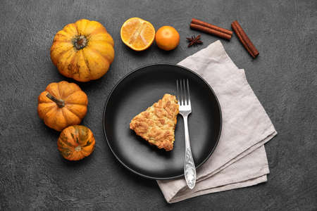 Plate with piece of tasty pumpkin pie and fresh vegetables on black backgroundの写真素材