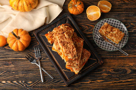 Plate and board with pieces of tasty pumpkin pie on wooden backgroundの写真素材