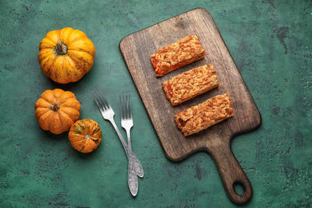 Wooden board with pieces of tasty pumpkin pie and fresh vegetables on green backgroundの写真素材