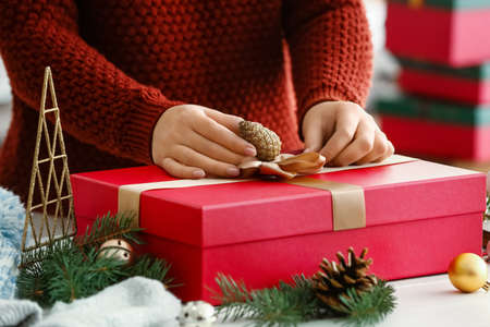 Woman decorating Christmas gift box at table in room, closeup