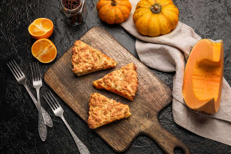 Wooden board with pieces of tasty pumpkin pie on black backgroundの写真素材