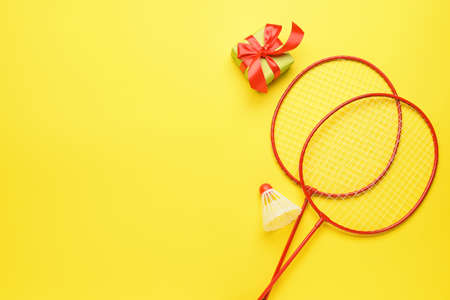 Badminton rackets, shuttlecock and Christmas gift on color background