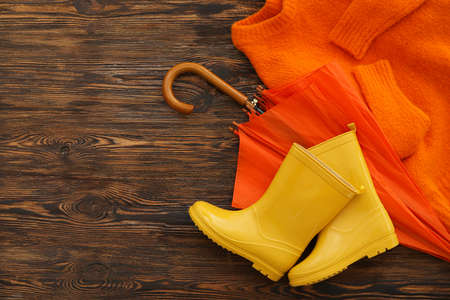 Umbrella, sweater and rubber boots on wooden backgroundの写真素材