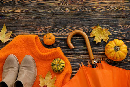 Composition with sweater, umbrella, shoes and autumn decor on dark wooden background, closeup