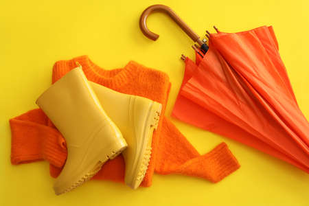 Rubber boots, umbrella and sweater on yellow backgroundの写真素材