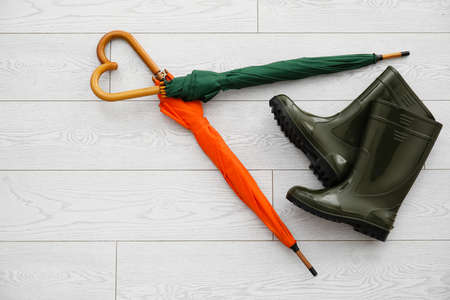 Composition with umbrellas and rubber boots on light wooden background