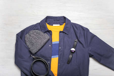 Stylish jacket, smartwatch, sweater, hat and belt on light wooden background