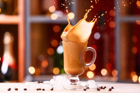 Glass cup of tasty iced coffee with splashes on table against blurred background
