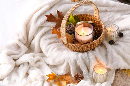 Burning candles in holders and autumn decor on soft plaid in room