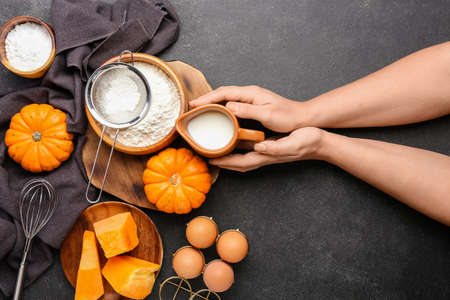 Female hands with fresh ingredients for preparing pumpkin pie on black backgroundの写真素材