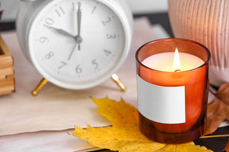 Burning candle in holder and autumn leaf on table in room