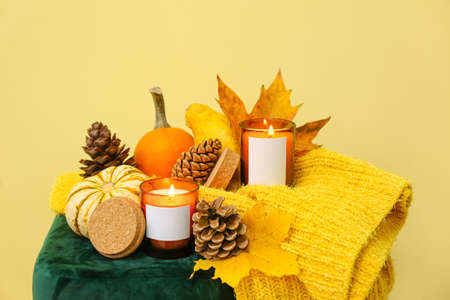 Burning candles in holders and autumn decor on pouf near yellow wallの写真素材