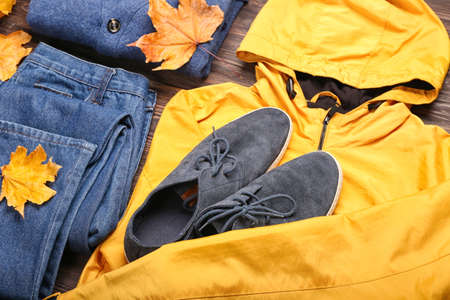 Stylish jacket, sweater, jeans, shoes and autumn leaves on wooden background, closeupの写真素材