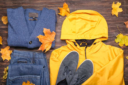 Stylish jacket, sweater, jeans, shoes and autumn leaves on wooden backgroundの写真素材