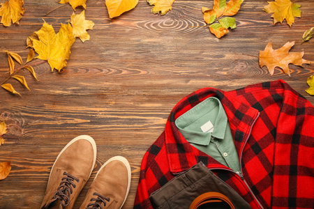 Stylish plaid jacket, shirt, pants, belt, shoes and autumn leaves on wooden backgroundの写真素材