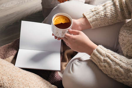 Woman sitting on sofa with book and holding cup of tea in living room, closeup