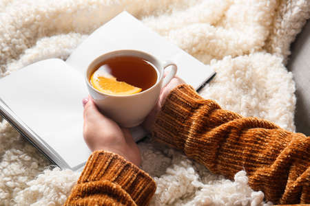 Woman holding cup of tea and opened book on fluffy plaidの写真素材