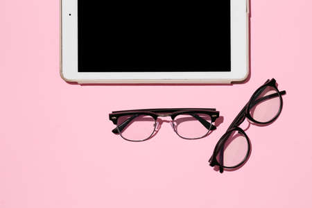 Stylish eyeglasses and tablet computer on pink backgroundの写真素材