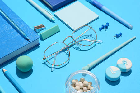 Stylish eyeglasses with stationery and cosmetic products on blue backgroundの写真素材