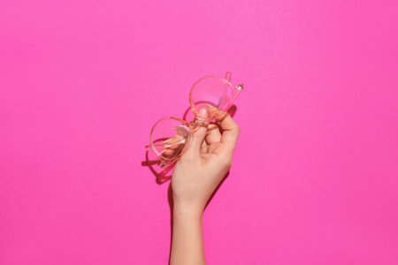 Female hand with stylish eyeglasses on pink backgroundの写真素材
