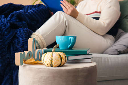 Pumpkin, stack of books and cup of tea on pouf near sofa in living roomの写真素材