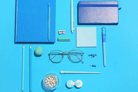 Stylish eyeglasses with stationery and cosmetic products on blue backgroundの写真素材